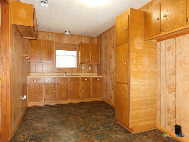 135 W Bayshore Dr, Palacios, TX 77465 - kitchen featuring wooden walls, brown cabinets, a sink, light countertops, and dark stone finish flooring