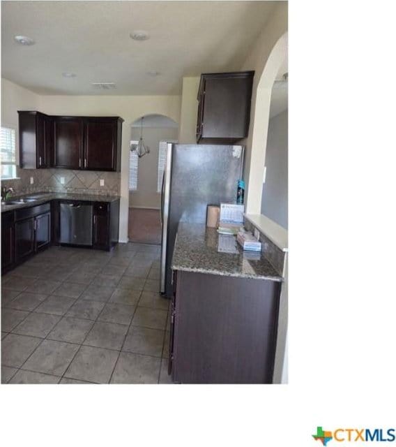 9511 Adeel Dr, Killeen, TX 76542 - kitchen with appliances with stainless steel finishes, arched walkways, backsplash, dark brown cabinets, and light tile patterned flooring