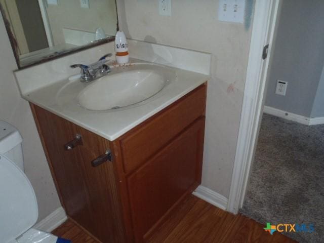 half bath with toilet, baseboards, and vanity