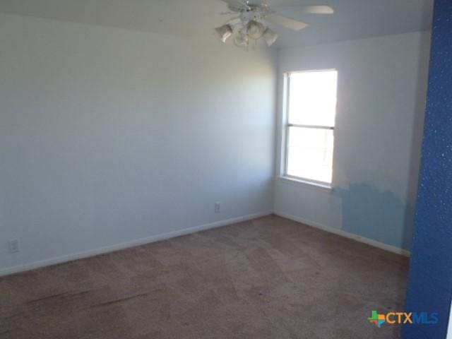 carpeted spare room featuring ceiling fan and baseboards