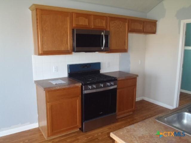 kitchen with a sink, stainless steel appliances, decorative backsplash, and wood finished floors