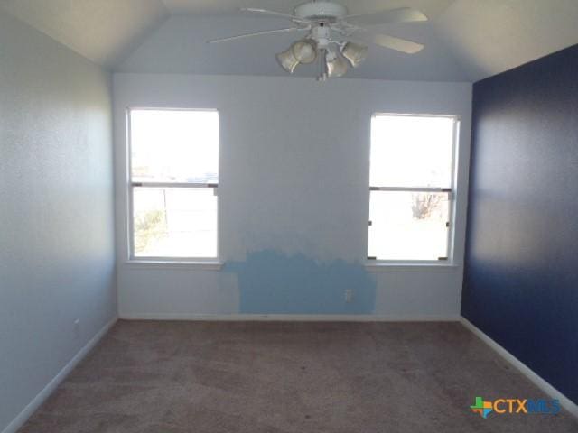 empty room featuring carpet flooring, vaulted ceiling, baseboards, and ceiling fan