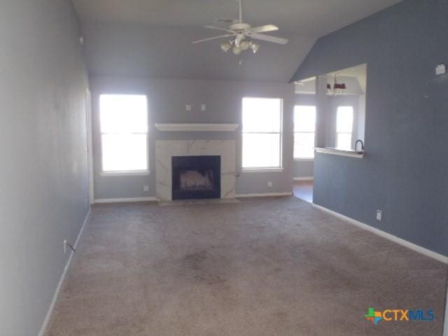 unfurnished living room with a high end fireplace, a wealth of natural light, carpet flooring, and lofted ceiling