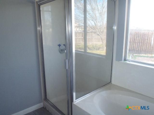 bathroom featuring a garden tub, a shower stall, baseboards, and a wealth of natural light