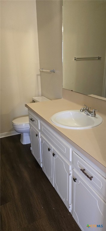 bathroom with baseboards, toilet, wood finished floors, and vanity