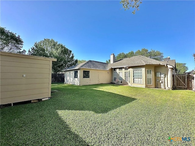 rear view of property featuring a yard, fence, and a chimney