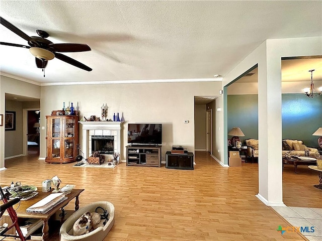 living area with light wood finished floors, a tile fireplace, ceiling fan with notable chandelier, and crown molding