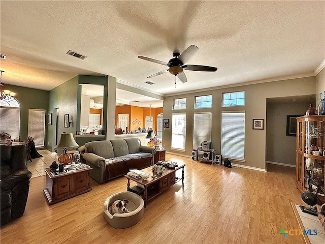 living room with light wood-type flooring, ceiling fan, visible vents, and a textured ceiling