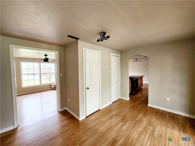 empty room with a ceiling fan, light wood-style flooring, arched walkways, and baseboards
