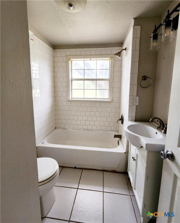 bathroom featuring vanity, toilet, a textured ceiling, tile patterned floors, and  shower combination
