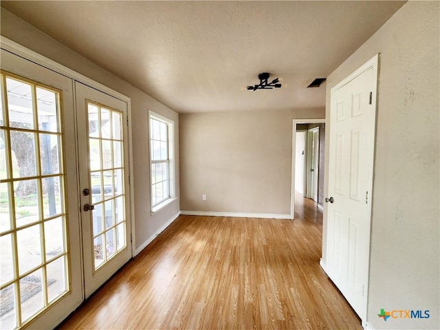 spare room featuring french doors, baseboards, a textured ceiling, light wood-style floors, and visible vents