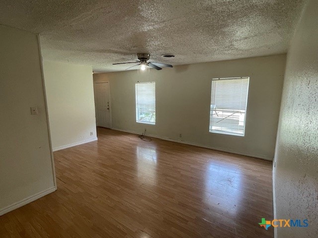 empty room with ceiling fan, plenty of natural light, wood-type flooring, and a textured ceiling