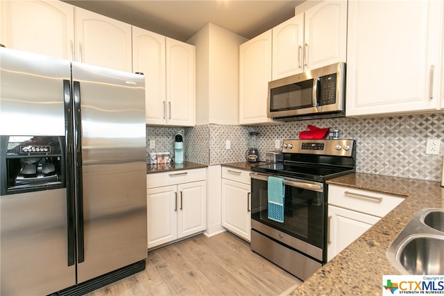 kitchen featuring dark stone countertops, white cabinetry, light hardwood / wood-style flooring, and appliances with stainless steel finishes