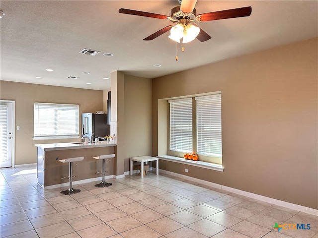 kitchen with light tile patterned floors, a breakfast bar, high quality fridge, kitchen peninsula, and ceiling fan