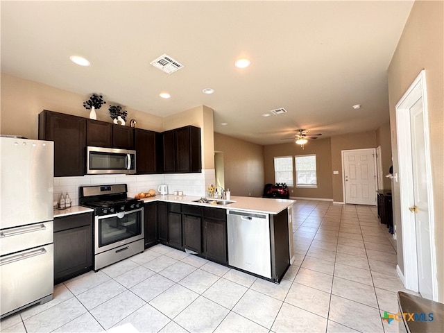 kitchen with stainless steel appliances, dark brown cabinetry, decorative backsplash, sink, and ceiling fan