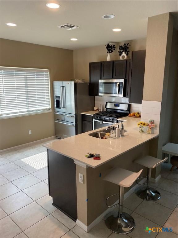 125 Duck Creek Trl, San Marcos, TX 78666 - kitchen with stainless steel appliances, light countertops, light tile patterned flooring, a sink, and a kitchen bar