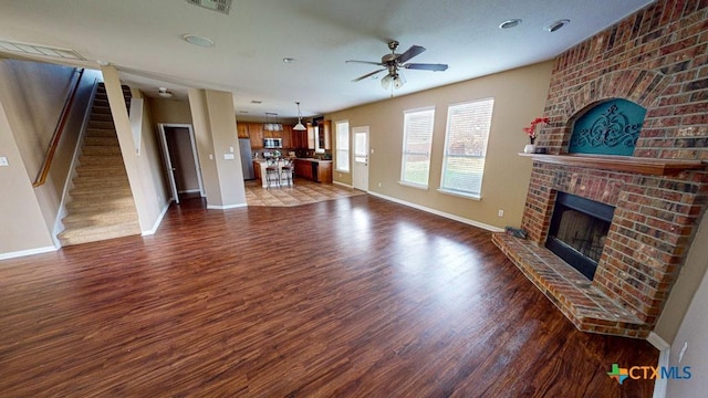 unfurnished living room featuring a brick fireplace, dark hardwood / wood-style floors, and ceiling fan