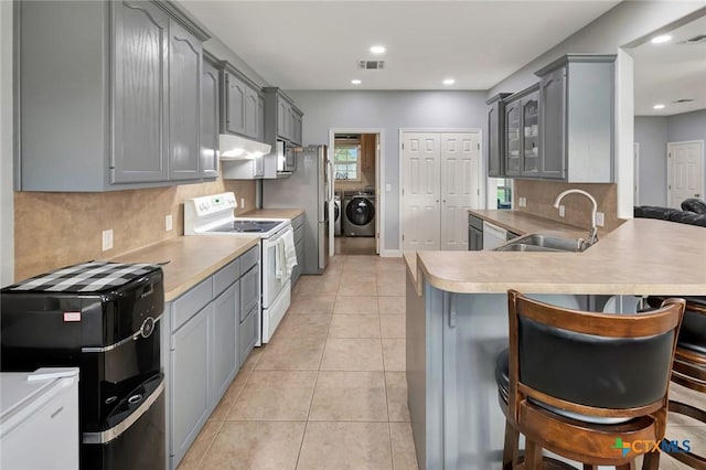 46 Bluestem St, Victoria, TX 77904 - kitchen featuring appliances with stainless steel finishes, washing machine and clothes dryer, under cabinet range hood, gray cabinets, and recessed lighting