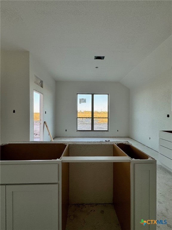 kitchen featuring white cabinets, vaulted ceiling, and a textured ceiling