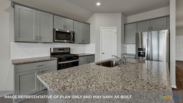 kitchen featuring an island with sink, sink, backsplash, light stone counters, and stainless steel appliances