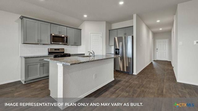 kitchen with sink, gray cabinets, appliances with stainless steel finishes, light stone countertops, and an island with sink