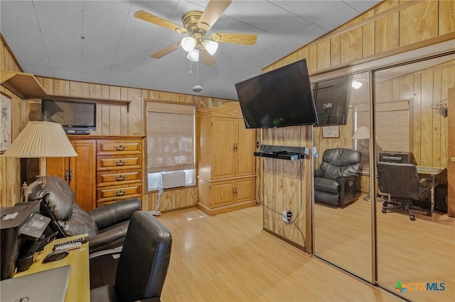 living room featuring light hardwood / wood-style flooring, ceiling fan, and wooden walls