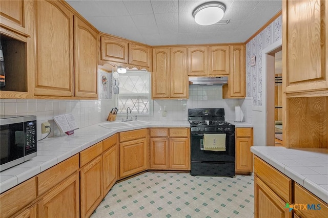 kitchen featuring black range with gas stovetop, backsplash, tile countertops, and sink