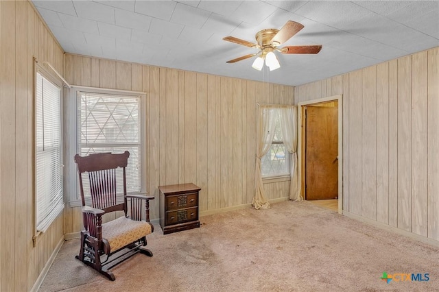 living area with ceiling fan, light carpet, and wooden walls