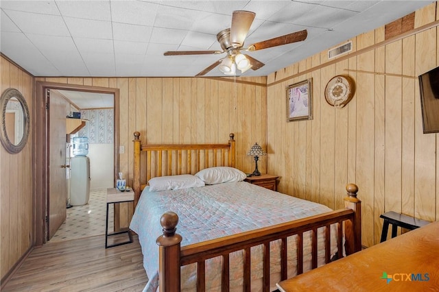 bedroom featuring ceiling fan, wooden walls, and light wood-type flooring