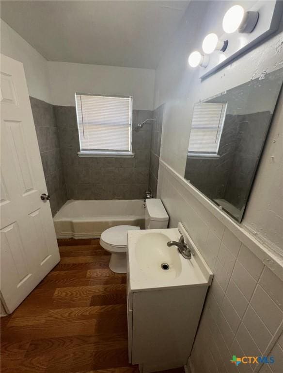 full bath with bathing tub / shower combination, toilet, tile walls, wood finished floors, and vanity