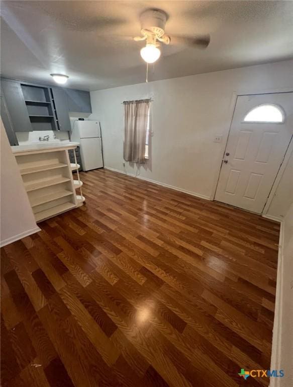 unfurnished living room featuring a ceiling fan, baseboards, and dark wood-type flooring
