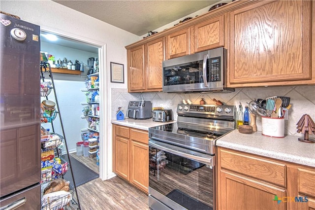 kitchen with tasteful backsplash, appliances with stainless steel finishes, light hardwood / wood-style flooring, and a textured ceiling