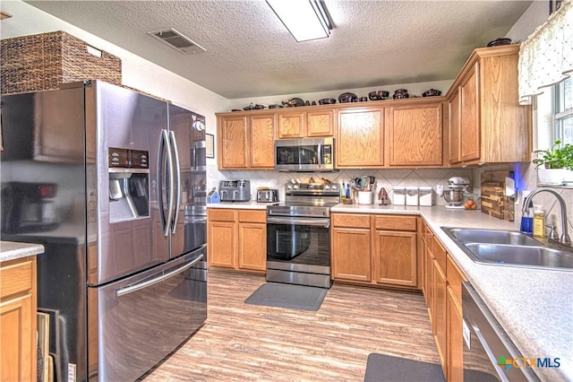 kitchen with stainless steel appliances, sink, decorative backsplash, and light wood-type flooring