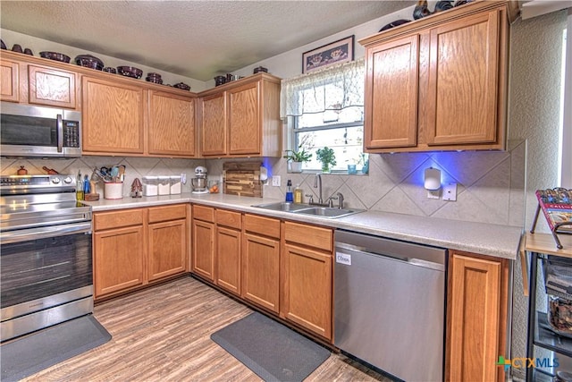 kitchen featuring sink, backsplash, stainless steel appliances, a textured ceiling, and light wood-type flooring