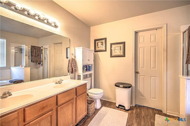 bathroom featuring wood-type flooring, vanity, walk in shower, toilet, and a textured ceiling