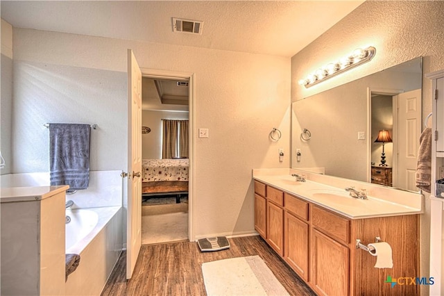 bathroom with vanity, wood-type flooring, a tub, and a textured ceiling