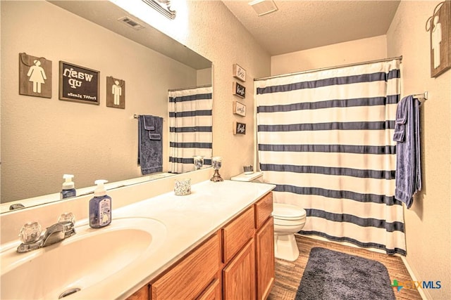 bathroom featuring wood-type flooring, toilet, vanity, and a textured ceiling