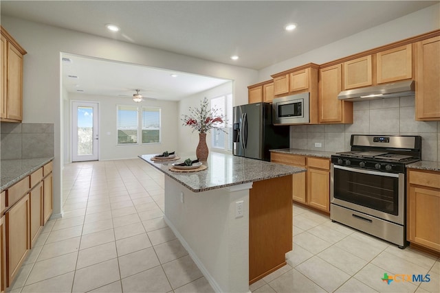 kitchen with light tile patterned flooring, appliances with stainless steel finishes, a center island, and stone counters