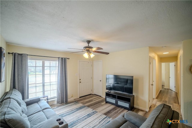 living room featuring ceiling fan, a textured ceiling, baseboards, and wood finished floors