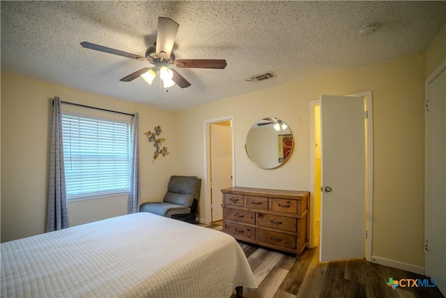 bedroom featuring visible vents, ceiling fan, a textured ceiling, wood finished floors, and baseboards