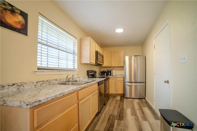 kitchen with stainless steel appliances, a sink, light countertops, light wood-type flooring, and light brown cabinetry