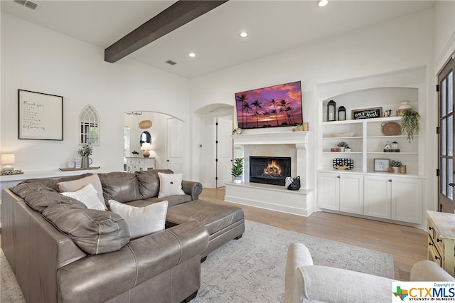 living room with built in shelves, light hardwood / wood-style flooring, and beamed ceiling