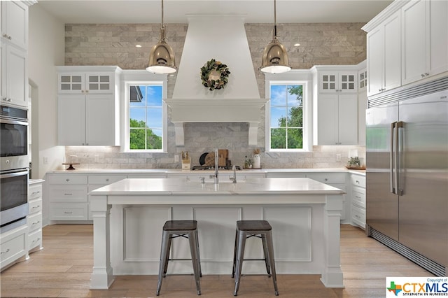 kitchen with appliances with stainless steel finishes, a kitchen island with sink, white cabinets, and decorative light fixtures