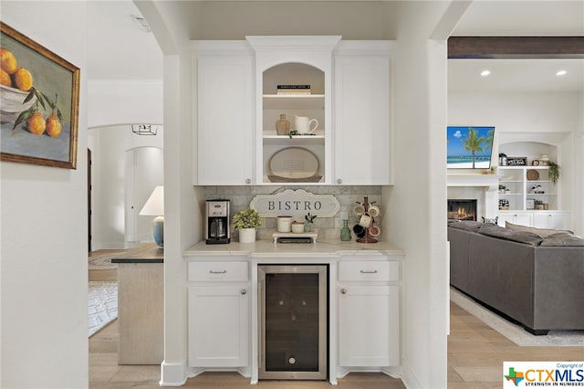 bar featuring white cabinetry, tasteful backsplash, light wood-type flooring, built in features, and beverage cooler