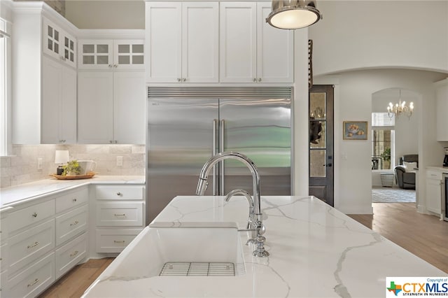 kitchen with light stone counters, decorative light fixtures, light hardwood / wood-style flooring, stainless steel built in fridge, and white cabinets