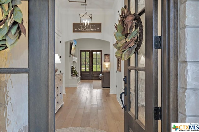 entryway with crown molding, a chandelier, light hardwood / wood-style floors, and french doors