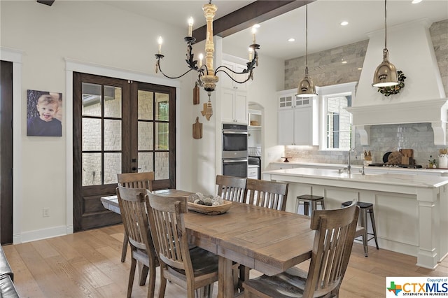 dining space featuring sink, light hardwood / wood-style flooring, an inviting chandelier, and french doors