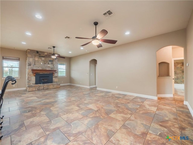 unfurnished living room featuring a stone fireplace and ceiling fan