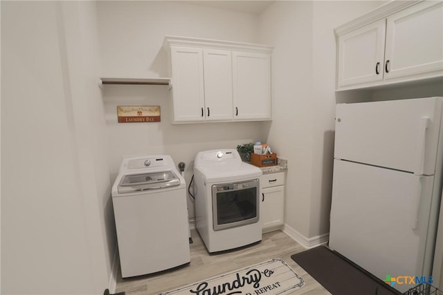 laundry area with washing machine and dryer, light wood-style floors, and cabinet space