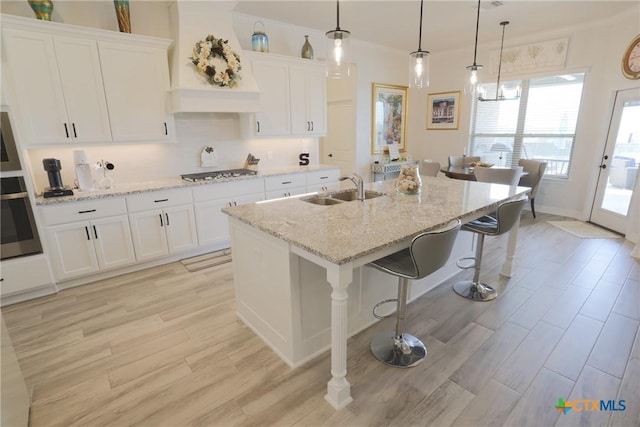 kitchen featuring light wood-style flooring, a sink, white cabinetry, appliances with stainless steel finishes, and premium range hood